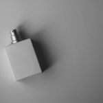 A sleek white perfume bottle photographed on a gray background with soft, muted lighting.